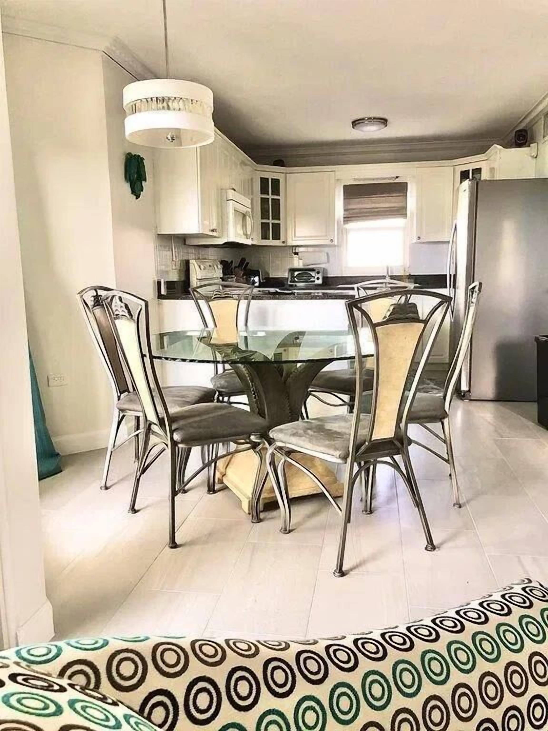 A modern kitchen with white cabinets, a central island, and a dining area with a glass table and metal chairs.
