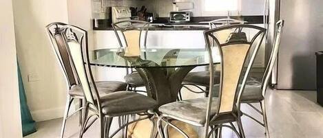 A modern kitchen with white cabinets, a central island, and a dining area with a glass table and metal chairs.