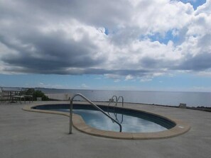 A swimming pool with a metal ladder, surrounded by a concrete deck, overlooking a body of water with a cloudy sky above. - Fabulous one Bedroom in West Bay (West Bay)
