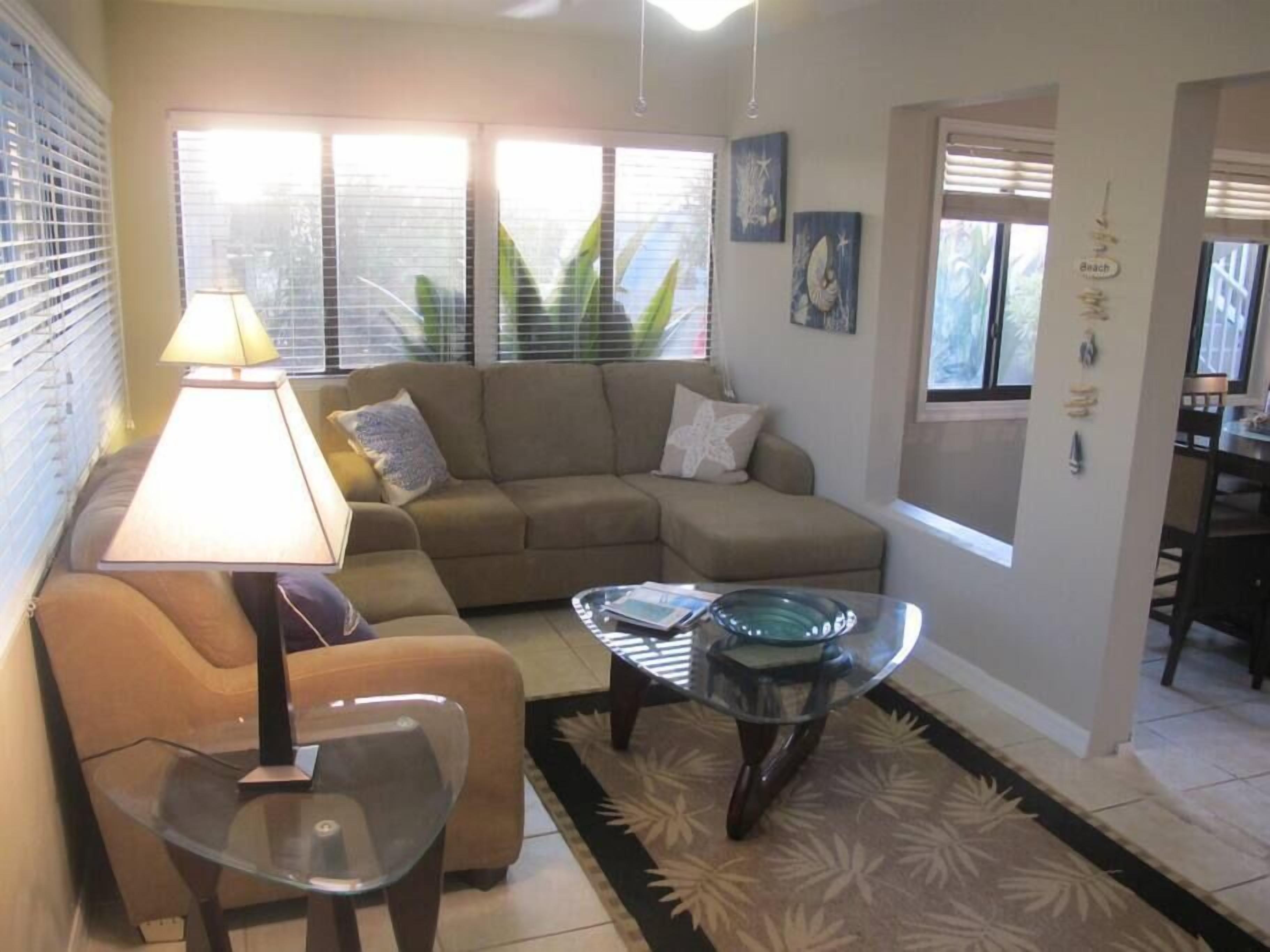 A living room with a sofa, a glass coffee table, a lamp, and a view of the outside through large windows.