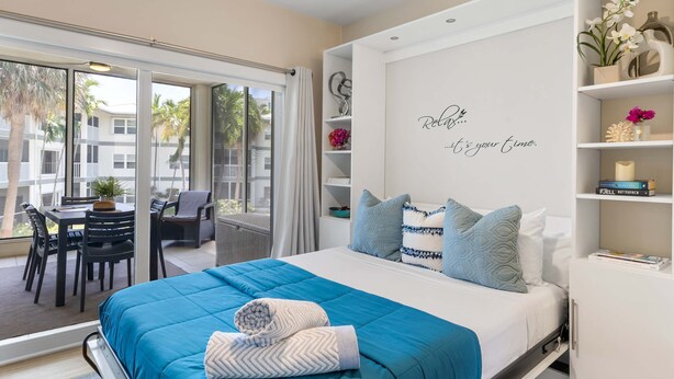 Ein modernes Hotelzimmer mit einem großen Bett, einem Balkon mit Sitzgelegenheit und einem an der Wand befestigten Regal mit Dekoration.