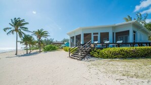 Een strandhuis met een overdekt terras, een trap naar de ingang en uitzicht op zee.
