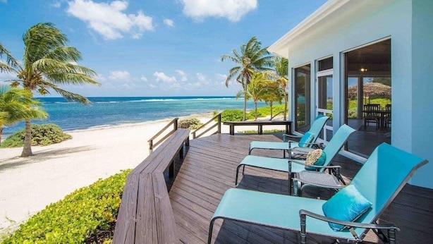 Een houten terras met lounge fauteuils met uitzicht op een strand en de oceaan.