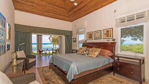Een slaapkamer met een groot bed, houten plafond en uitzicht op de oceaan.