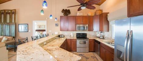 A kitchen with wooden cabinets, a granite countertop, stainless steel appliances, and a ceiling fan.