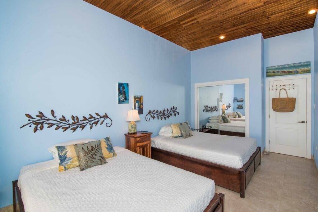 A bedroom with two beds, a wooden ceiling, and a mirror reflecting a room with a bed.