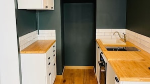 Eine kleine Küche mit weißen Schränken, Holz Arbeitsplatten und einer dunklen Wand.