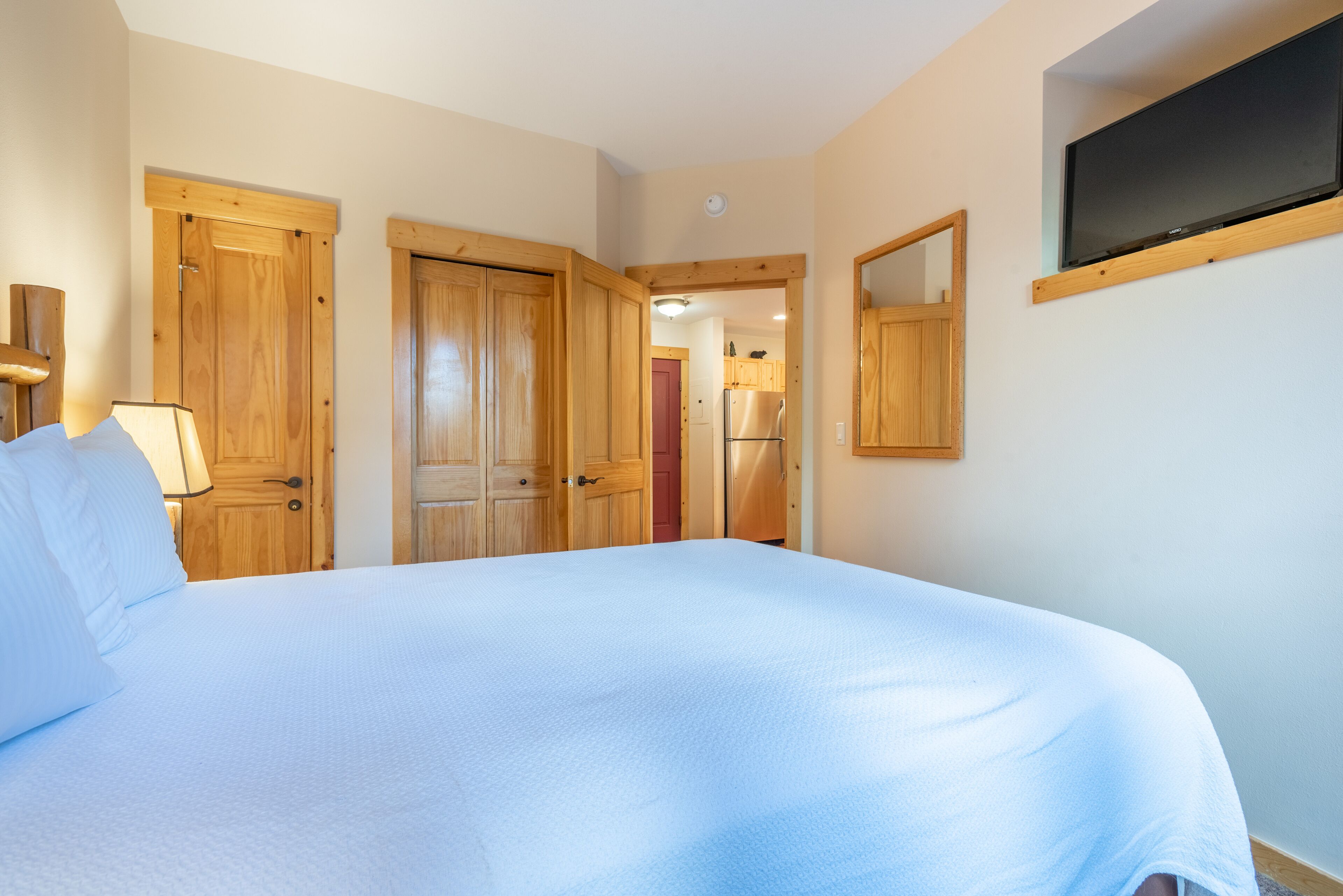 Un dormitorio con una cama grande, puertas de madera, un espejo y un televisor montado en la pared.