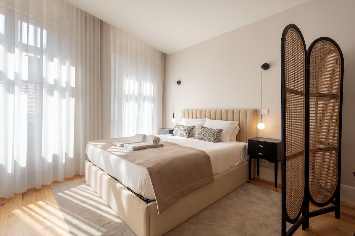 A modern bedroom with a large bed, bedside tables, a nightstand, and a decorative rattan partition.