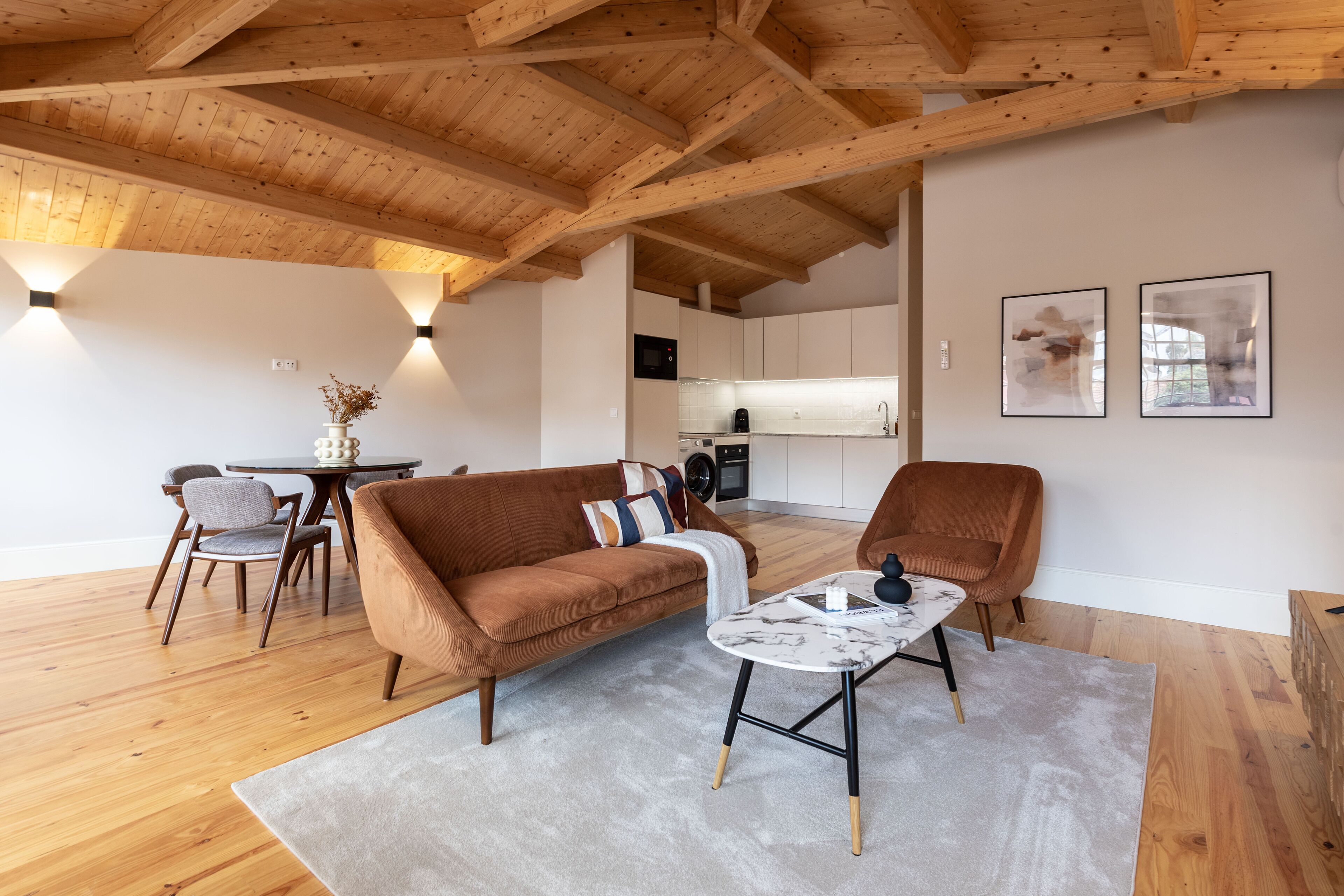 Una sala de estar moderna con techo de madera, un sofá marrón, una mesa de centro de mármol y un comedor con sillas y una mesa.