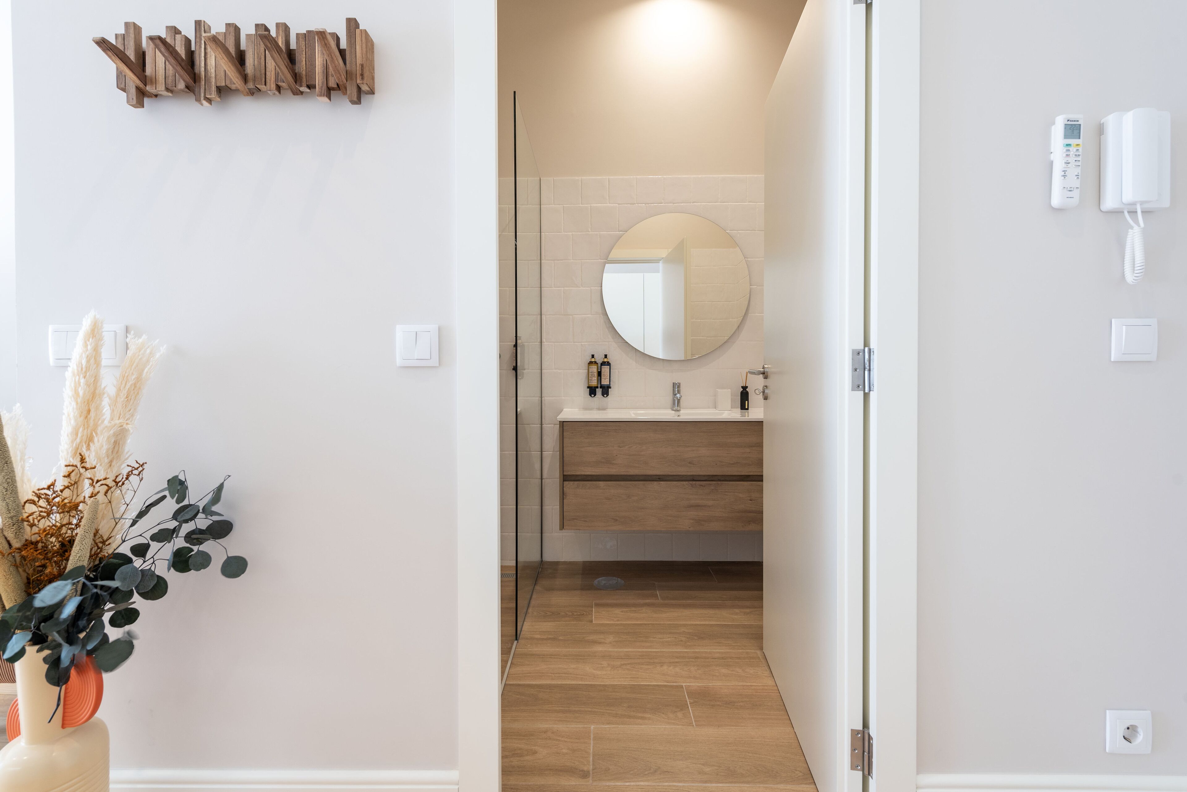 A modern bathroom with a wooden vanity, a round mirror, and a glass shower enclosure.