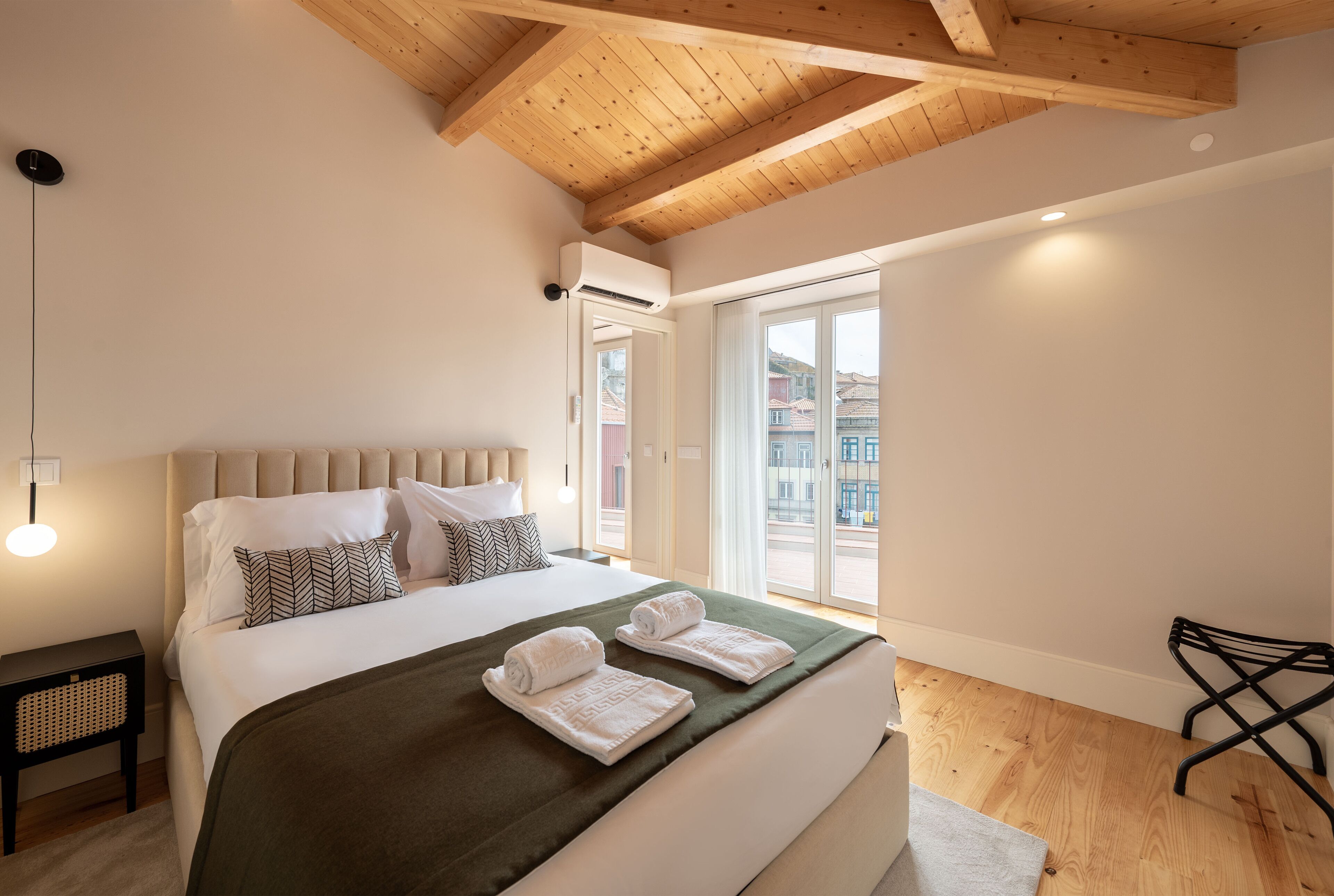 Une chambre d’hôtel moderne avec un grand lit, un plafond en bois et une vue sur la ville grâce à une grande fenêtre.