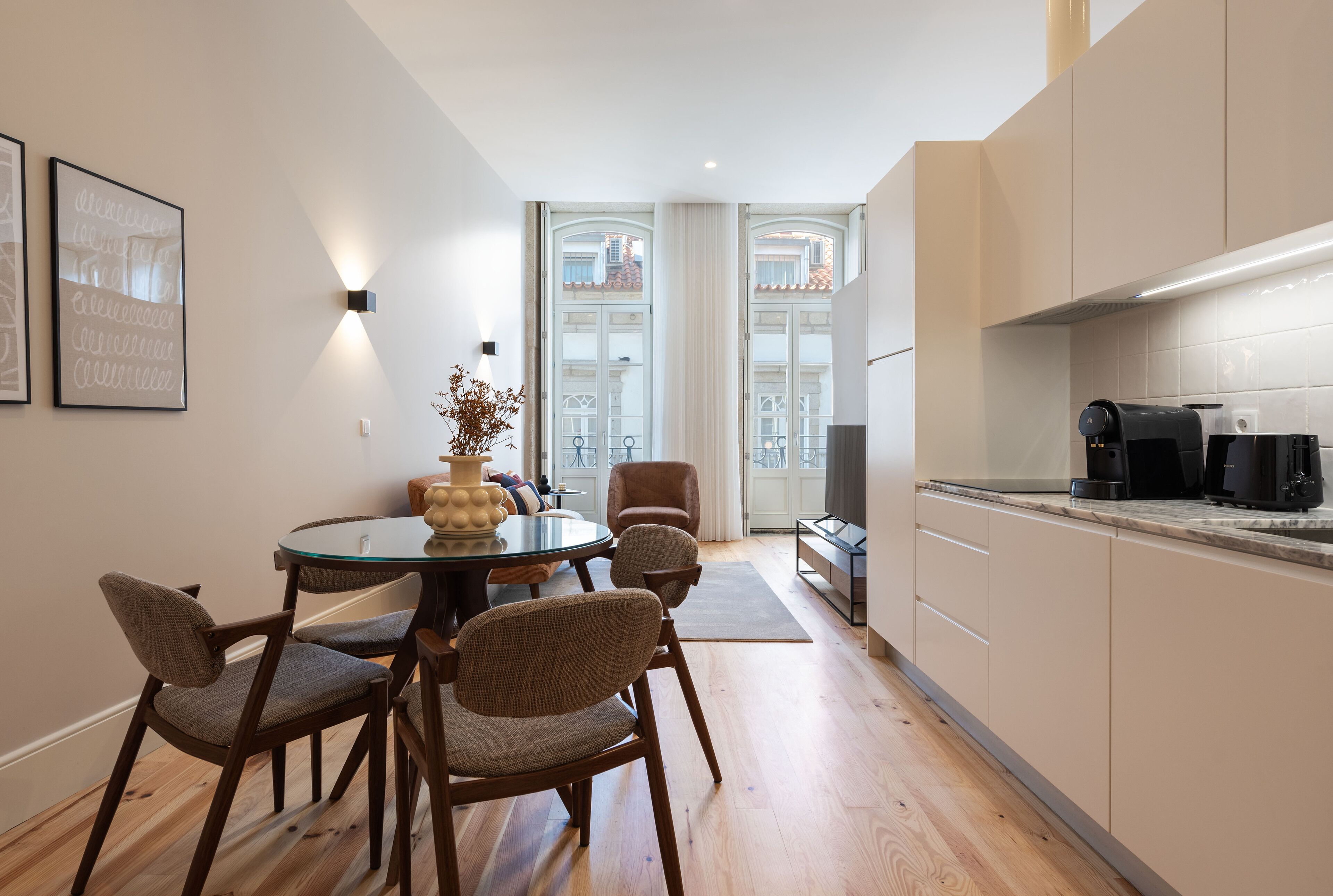 Eine moderne Küche mit Holzausstattung, einem Essbereich mit rundem Tisch und Stühlen sowie Blick durch große Fenster.
