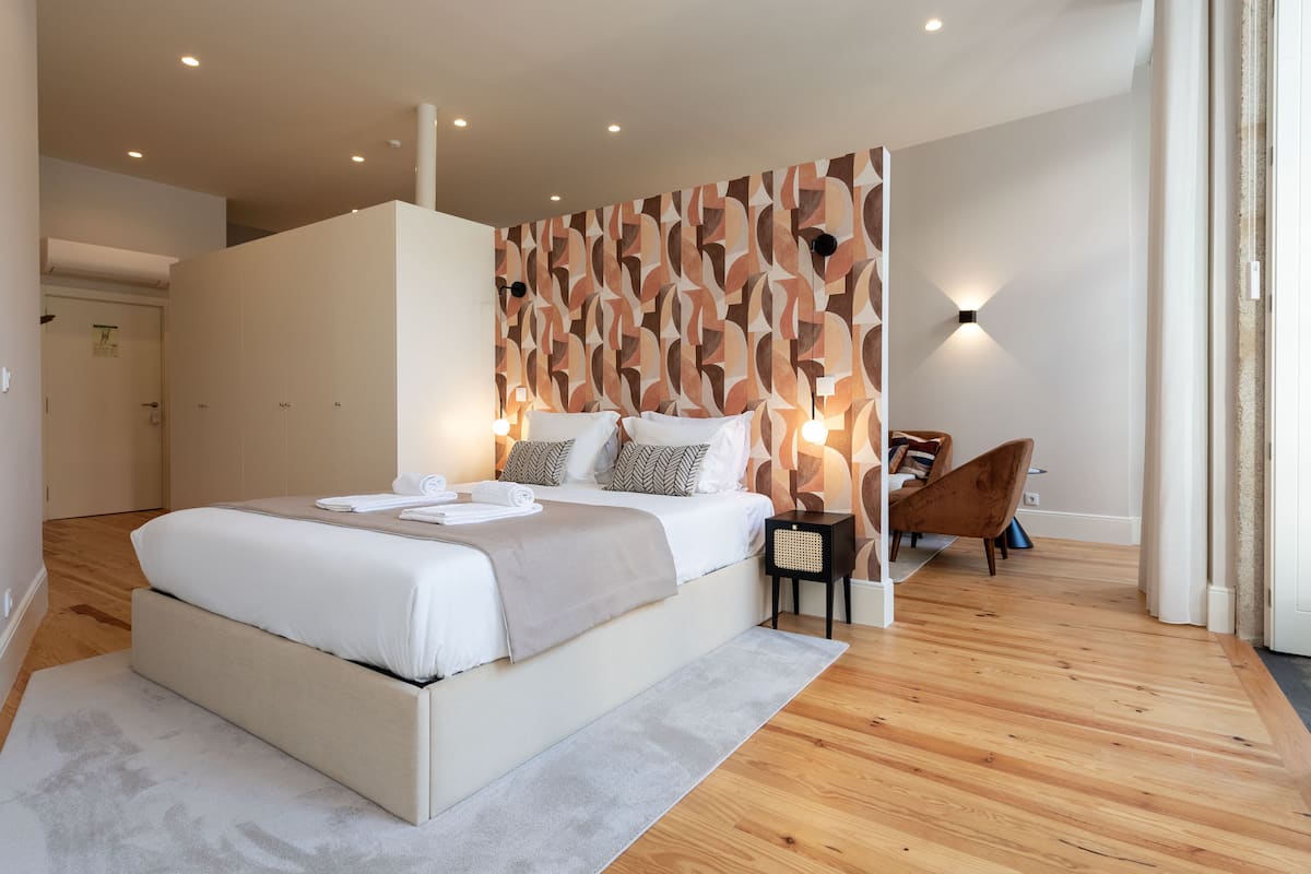 A modern bedroom with a large bed, a patterned wall, and a small seating area.