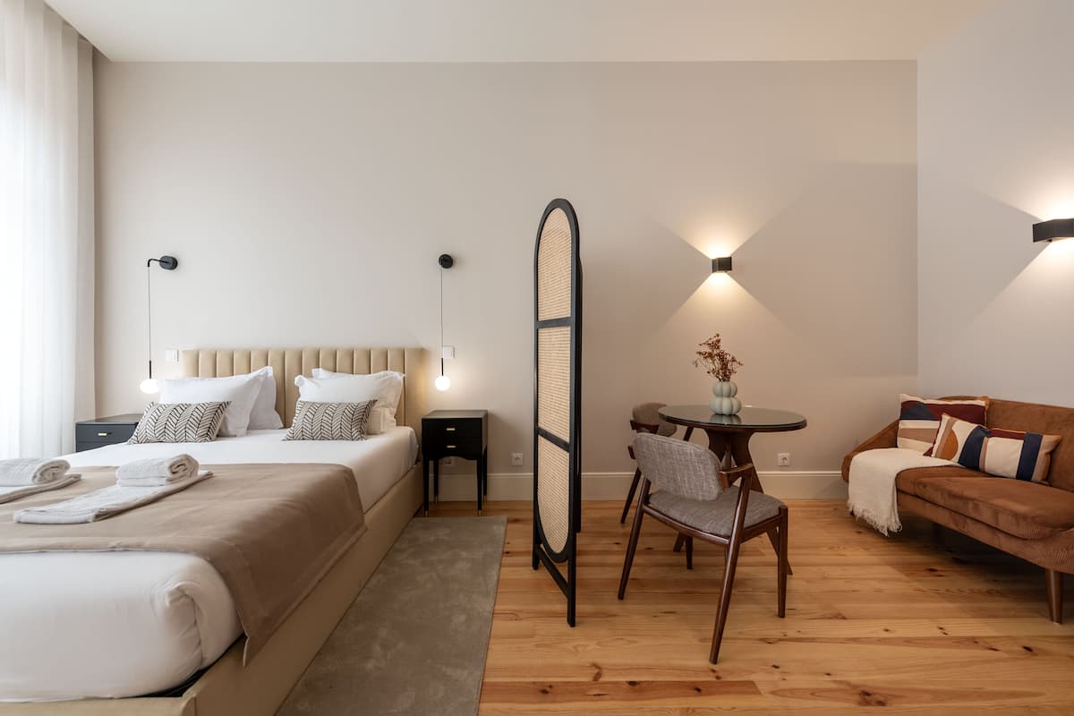 A modern hotel room with a bed, a seating area with a table and chairs, and a sofa.