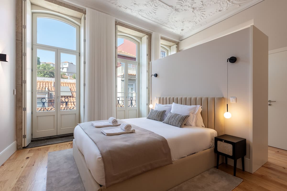 A bedroom with a large bed, a nightstand, and a view of the outside.