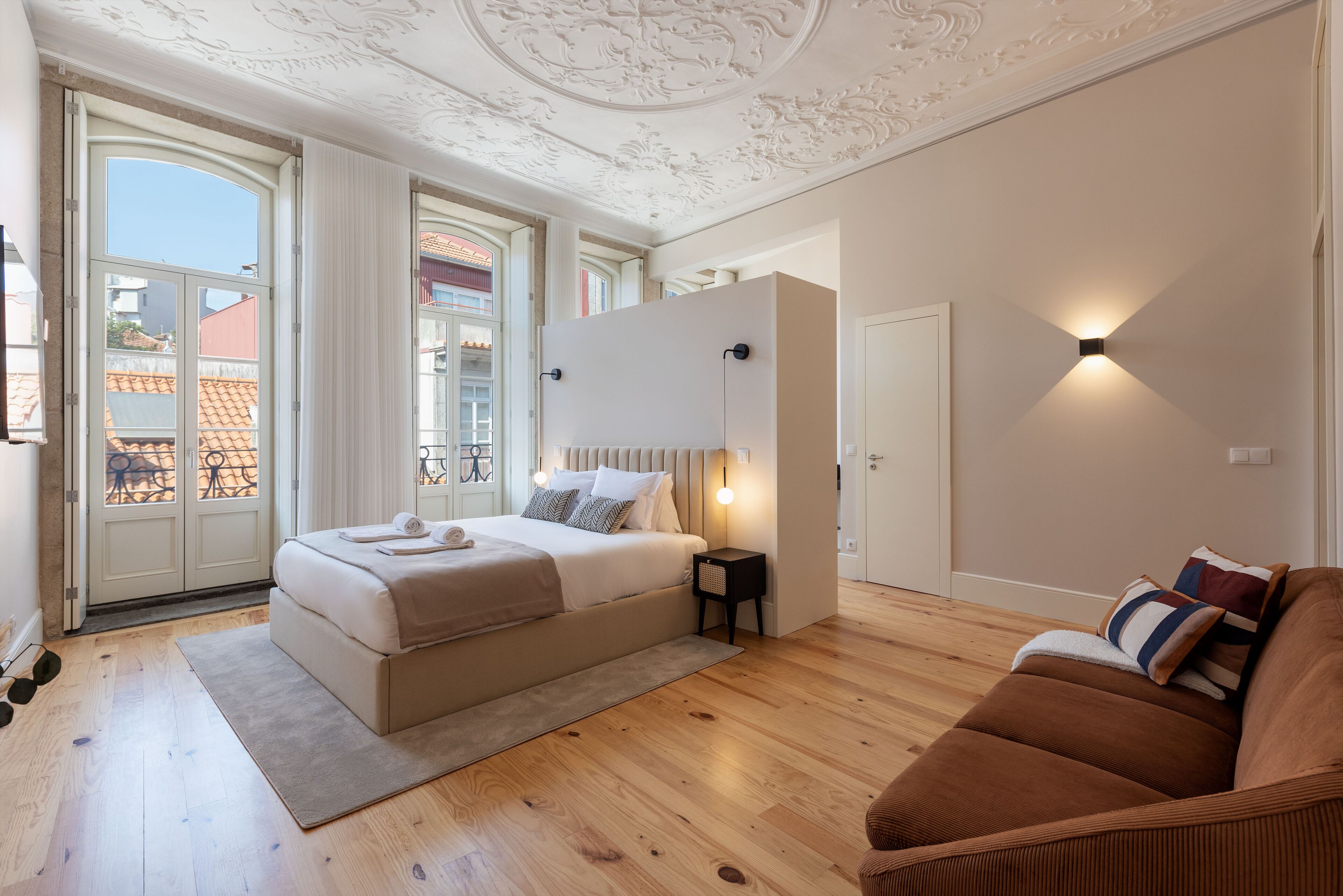 Un dormitorio con una cama grande, un sofá marrón, una mesita de noche y una lámpara de pared.
