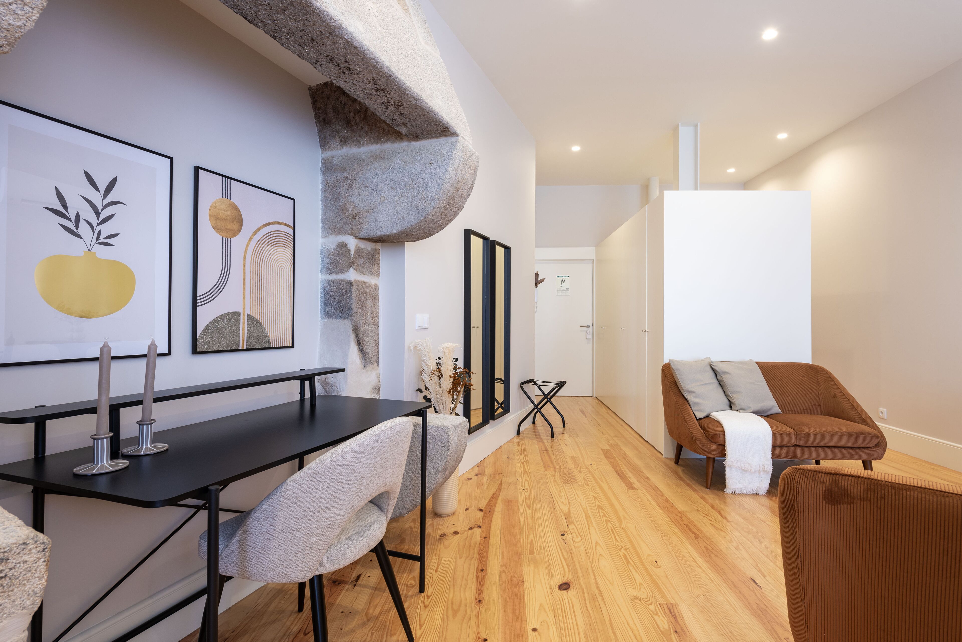 A modern living room with a wooden floor, a black dining table with two chairs, a brown sofa, and artwork on the wall.
