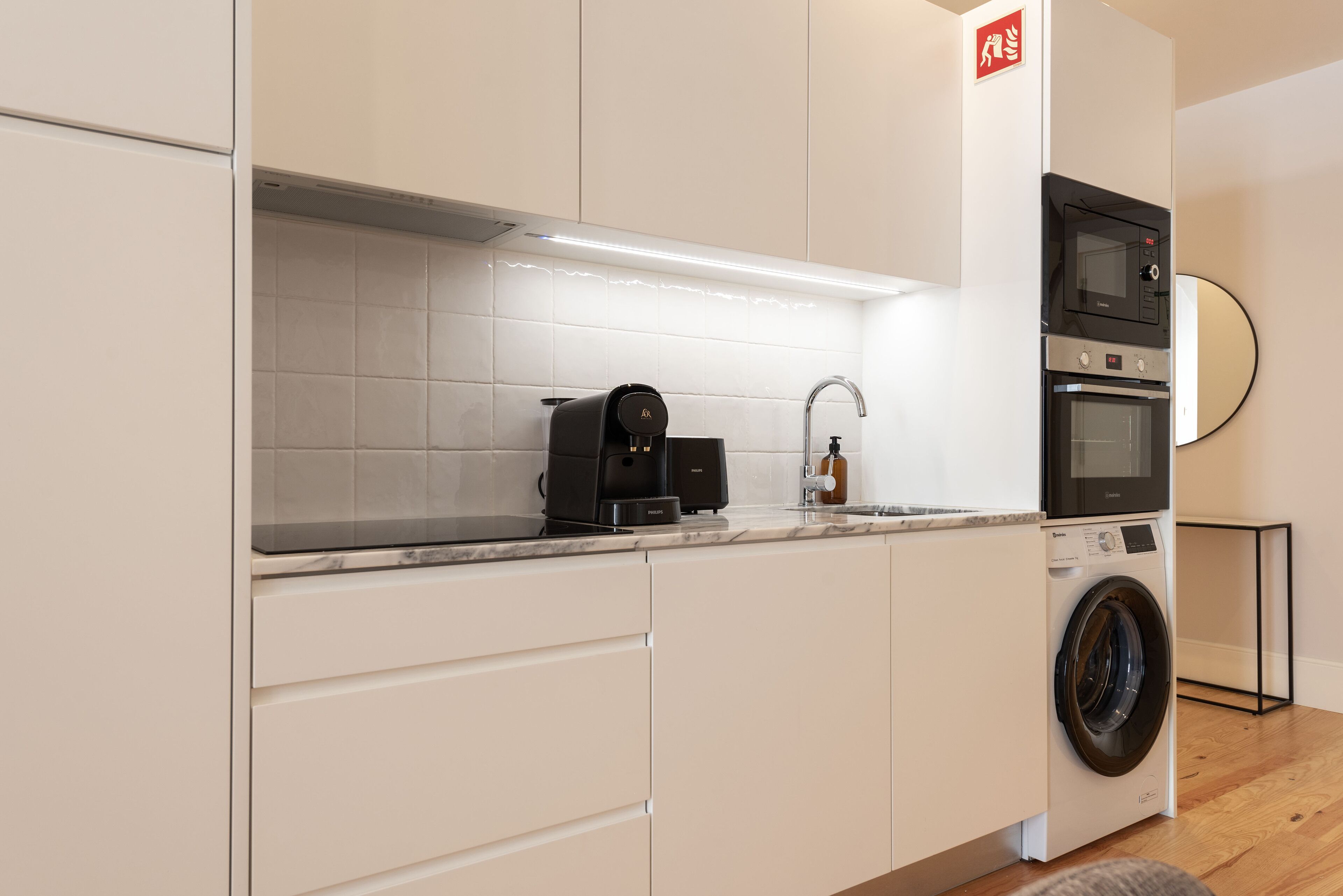 A compact kitchen with a built-in washing machine, a coffee maker, and a microwave.