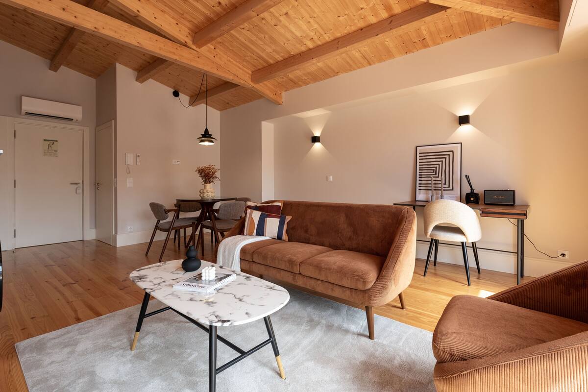 A modern living room with a wooden ceiling, a brown sofa, a white coffee table, and a desk with a computer.