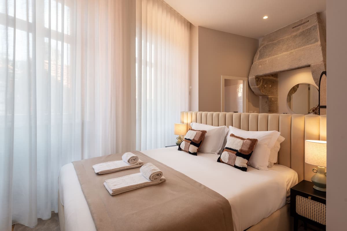 A hotel room with a large bed, two bedside lamps, a mirror, and a window with sheer curtains.
