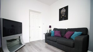 A modern living room with a flat-screen TV, grey sofa with colorful cushions, and a framed artwork on the wall. - Rugby Road by Tŷ SA (Newport)