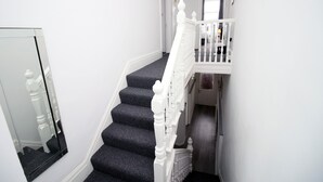 A staircase with dark carpeted steps and white balusters, leading to a landing with a door and a small window. - Rugby Road by Tŷ SA (Newport)