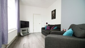 A living room with a grey sofa, a television, and a white door. - Rugby Road by Tŷ SA (Newport)