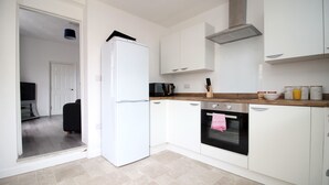 A modern kitchen with white cabinets, a black oven, and a white refrigerator. - Rugby Road by Tŷ SA (Newport)