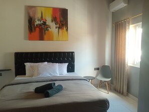 Ein Hotelzimmer mit einem Bett, einem Bild an der Wand, einem Sessel und einem Fenster mit Vorhängen.