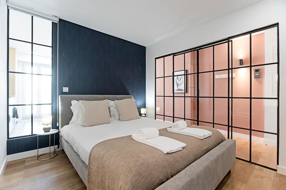 A modern hotel room with a large bed, a small bedside table, a window, and a sliding door.