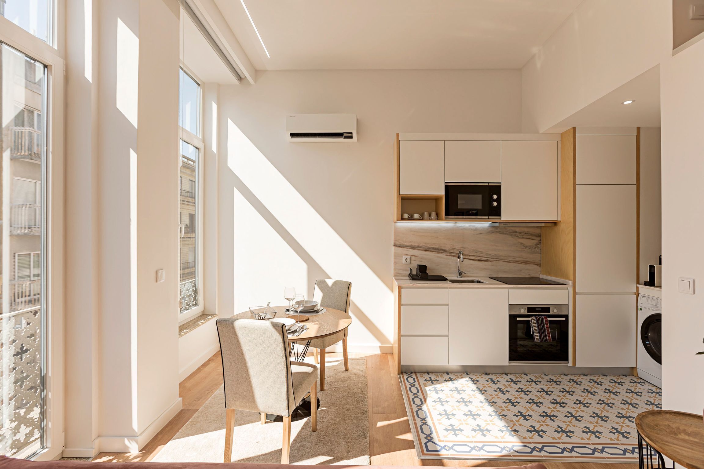 Een moderne keuken met inbouwapparatuur, een eethoek met tafel en stoelen, en een kamerbreed tapijt met dessin.