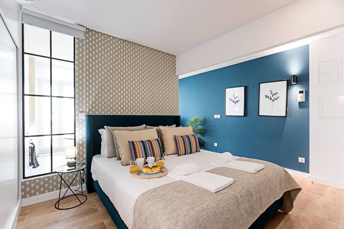 A modern bedroom with a large bed, a window with a view, and a breakfast tray on the bed.