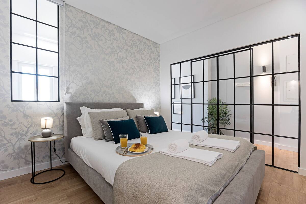 A modern bedroom with a large bed, a bedside table with a lamp, a tray with breakfast, and a sliding door with a view.
