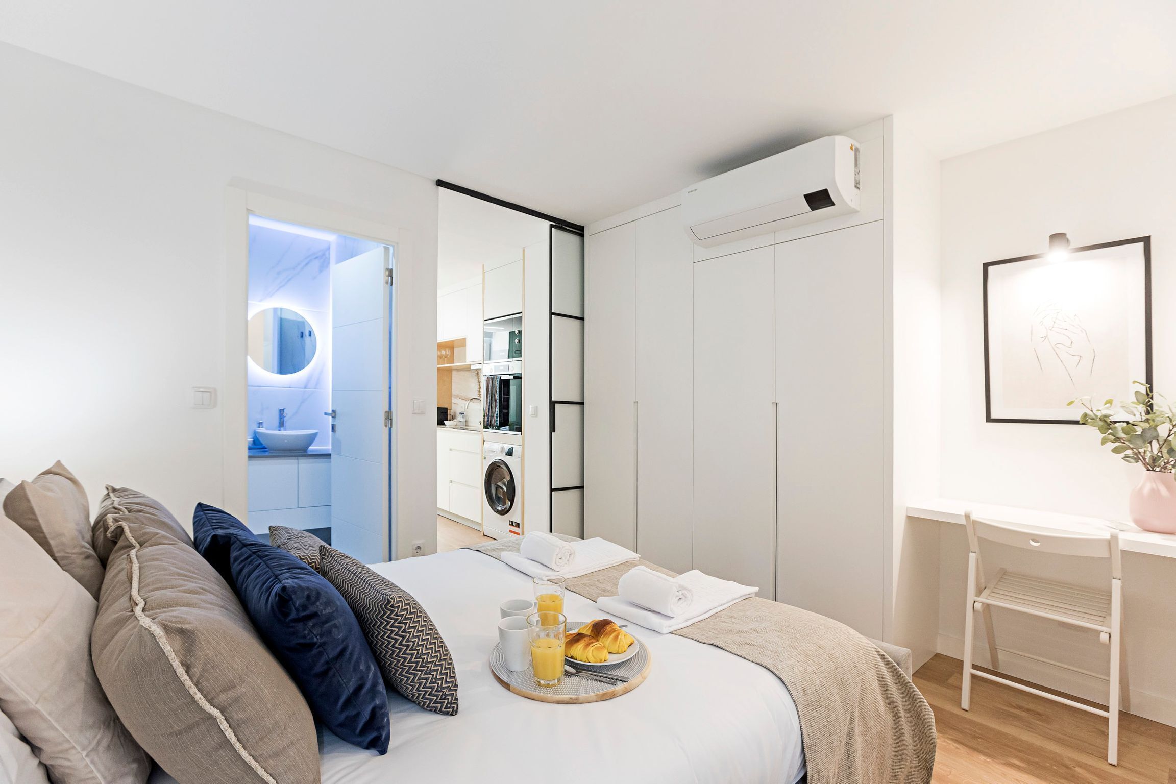 A modern hotel room with a bed, breakfast tray, and a view of the bathroom and kitchen.