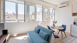 En moderne stue med sofa, spisebord og stole. Store vinduer giver udsigt over bybilledet.