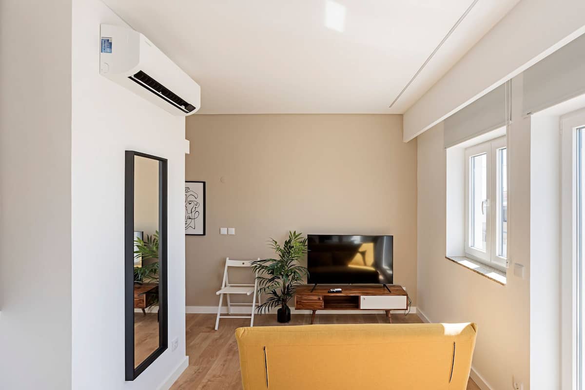 A living room with a TV, a sofa, a plant, and a window.
