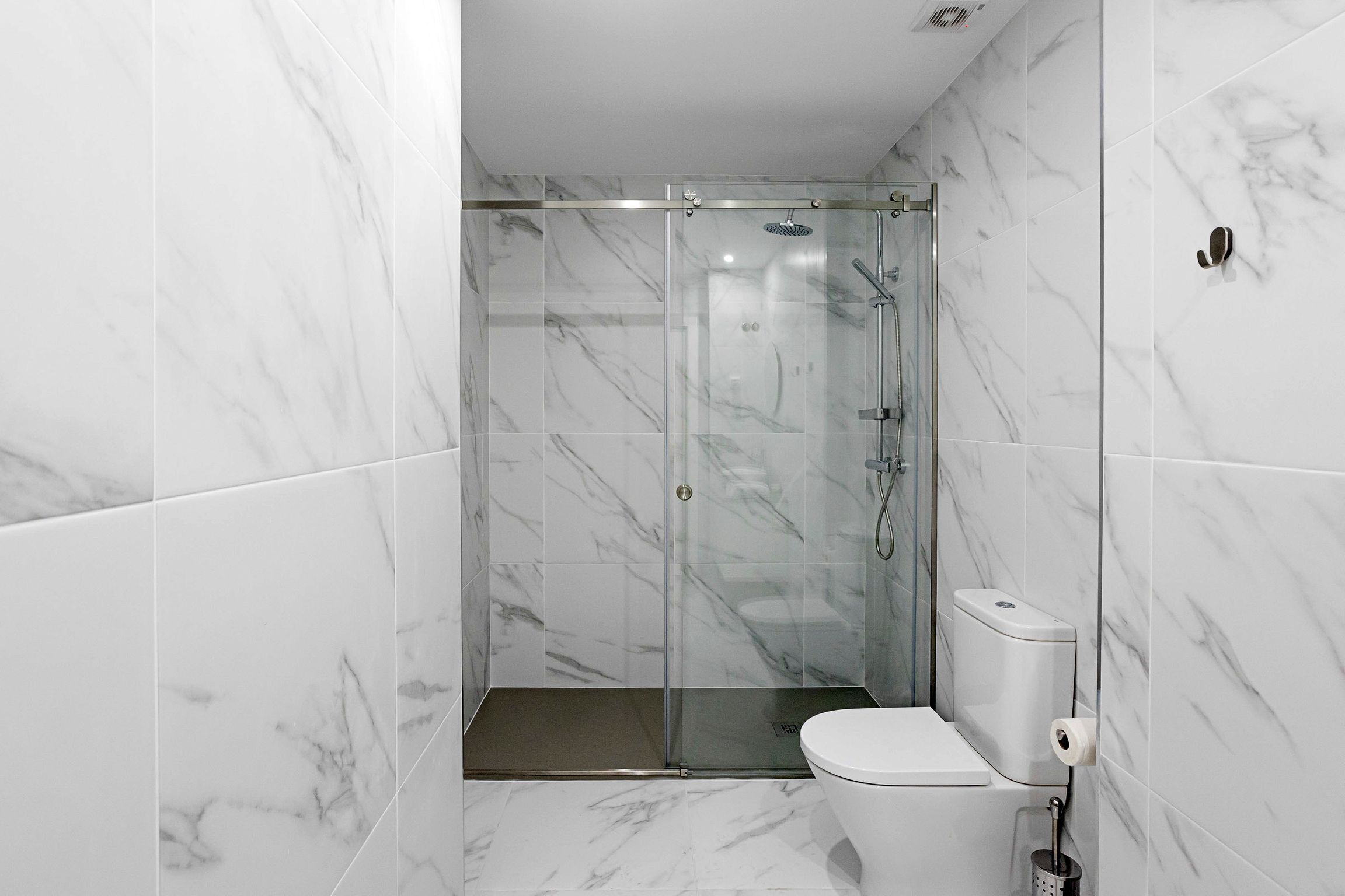 A modern bathroom with a glass-enclosed shower, a toilet, and a marble-tiled floor.