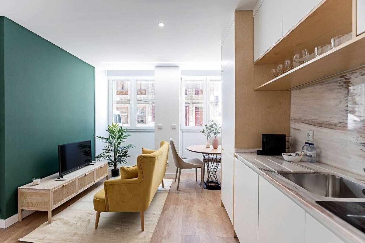A modern living space with a TV, sofa, dining table, and kitchen area.