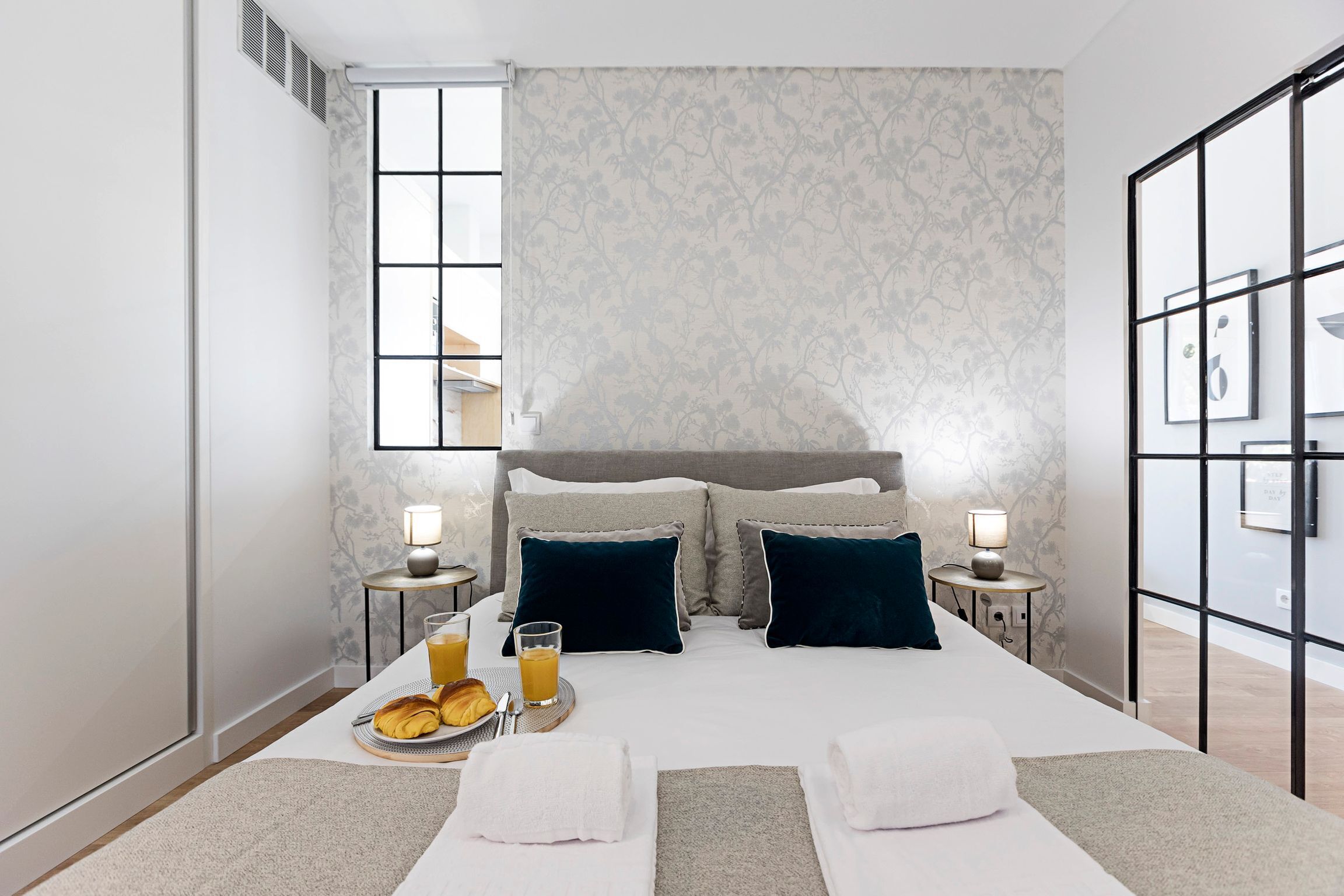 A modern hotel room with a large bed, two bedside tables, a window, and a view of the city.