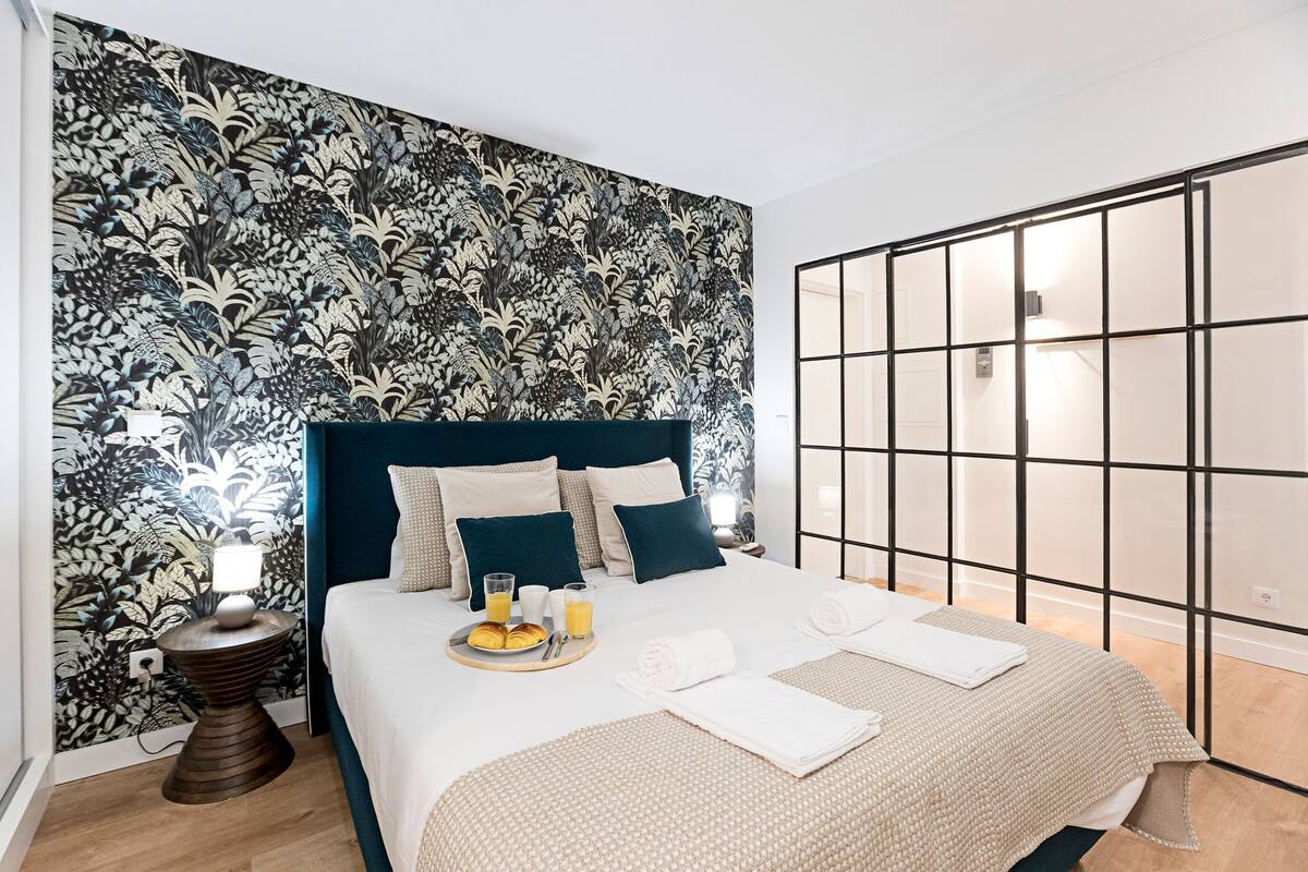 A neatly made bed with a blue headboard, a bedside table with a lamp, and a tray with breakfast items.