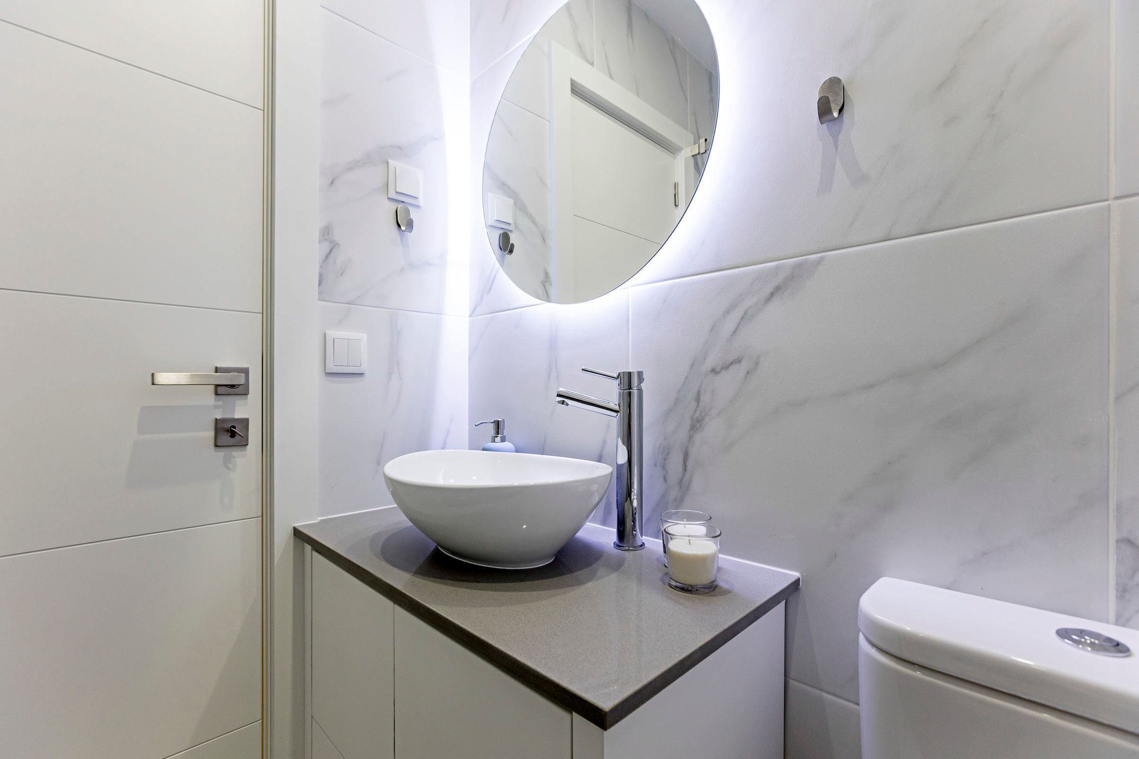 Une salle de bain moderne avec un lavabo en marbre blanc, un miroir rond et des toilettes.
