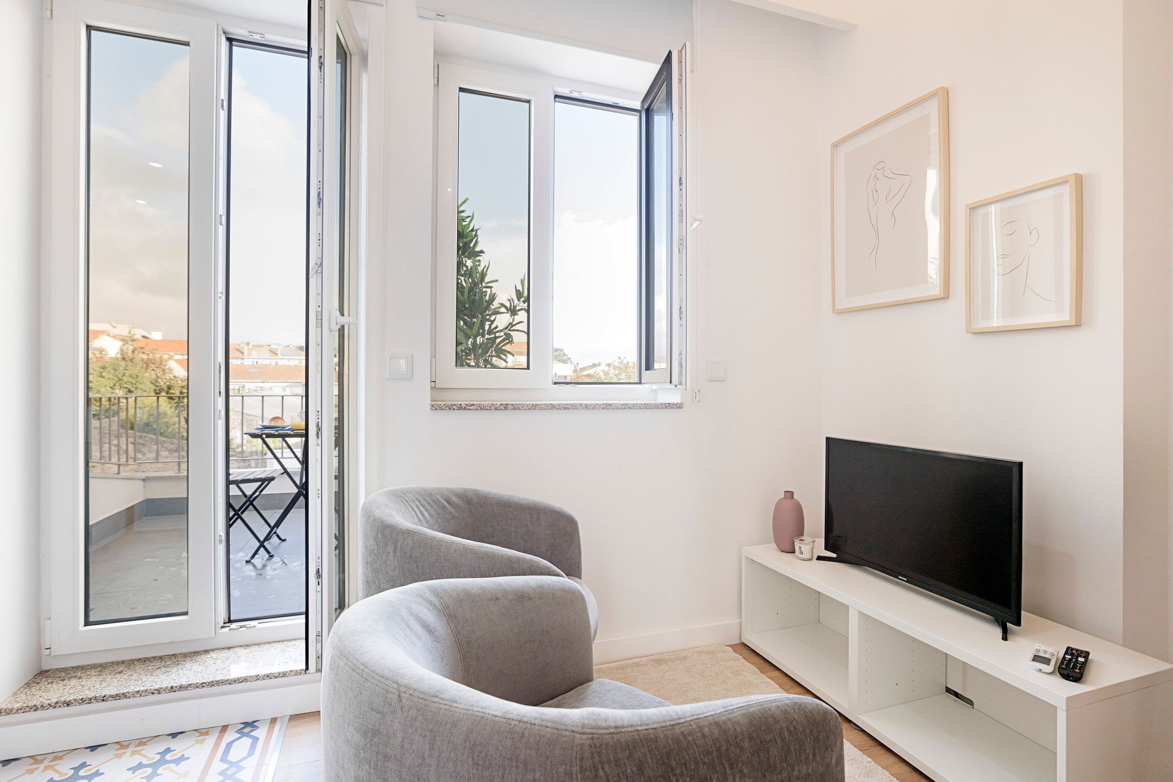 A modern living room with a grey sofa, a flat-screen TV on a white stand, and two framed artworks on the wall.
