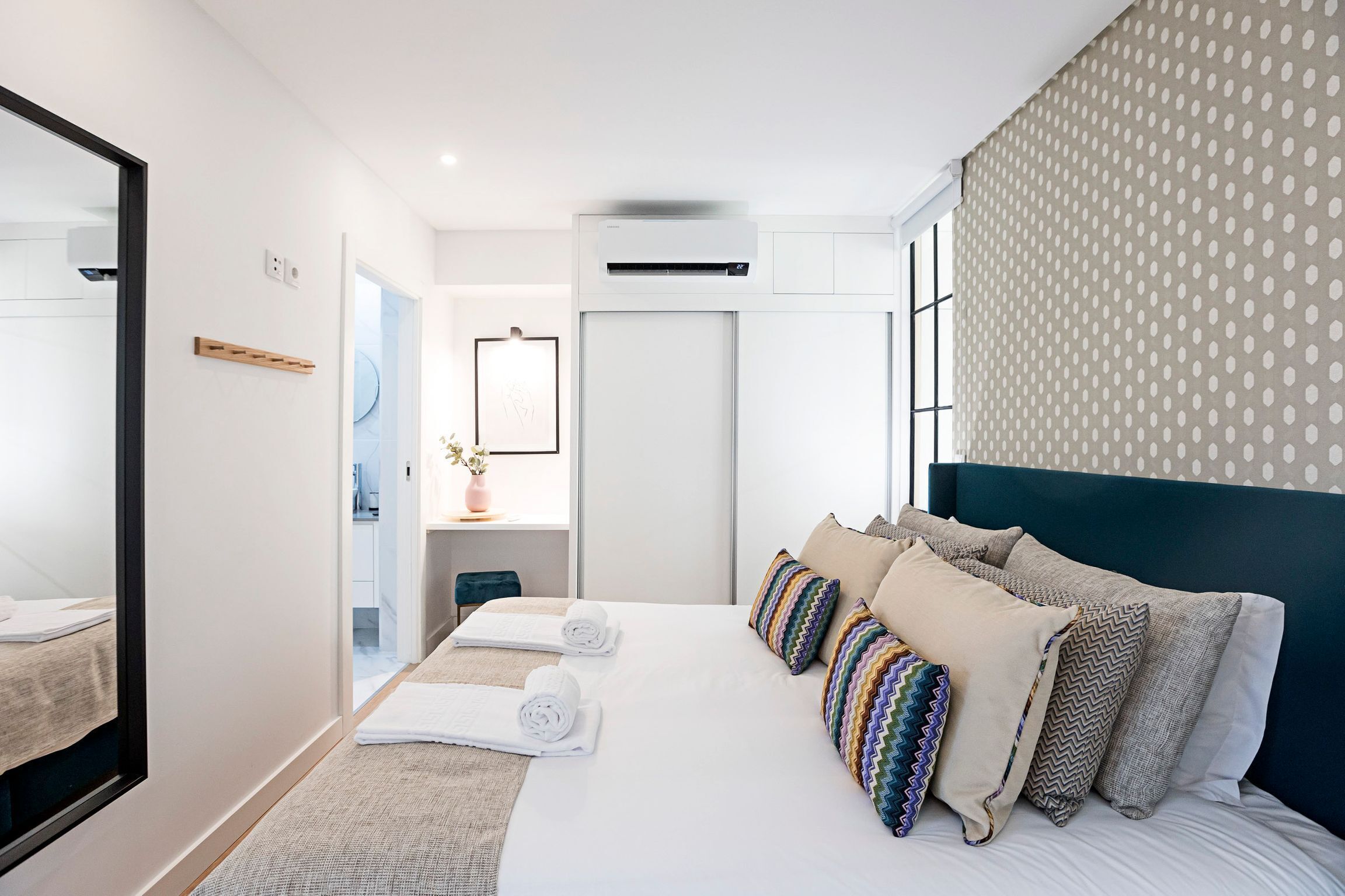 Une chambre d’hôtel moderne équipée d’un grand lit, d’une table de chevet, d’un miroir et d’un appareil de climatisation.