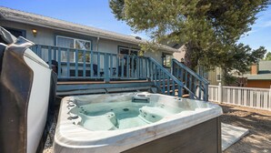A hot tub in a backyard with a wooden deck and stairs leading to a house.