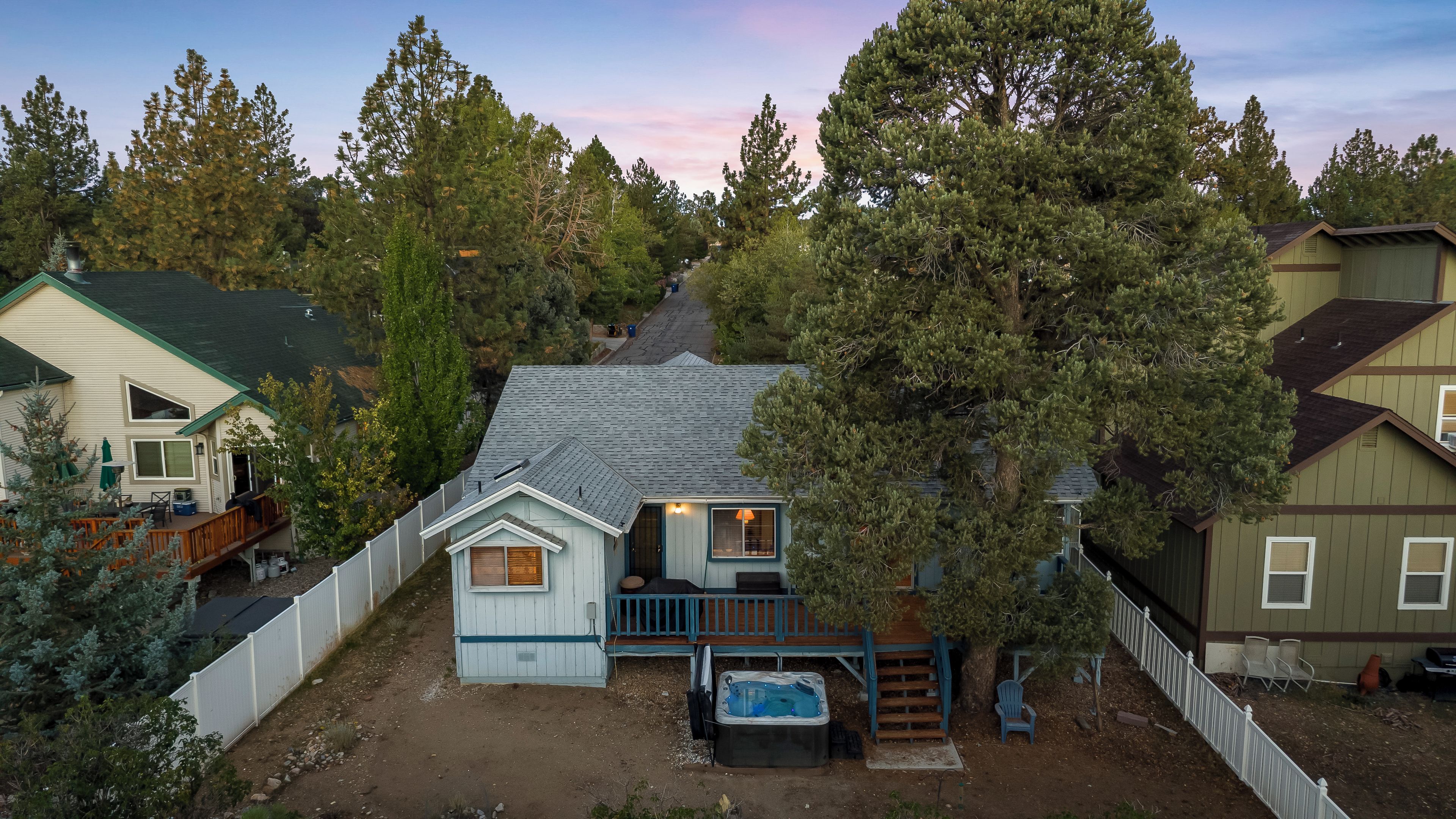 A residential property with a detached house featuring a deck, a hot tub, and a fenced yard.