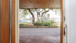 An open doorway leading to a paved outdoor area with a tree and a metal fence. - Beach Shack Fremantle (Fremantle)
