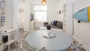 A room with a round table, a sofa, a TV, and a surfboard on the wall. - Beach Shack Fremantle (Fremantle)