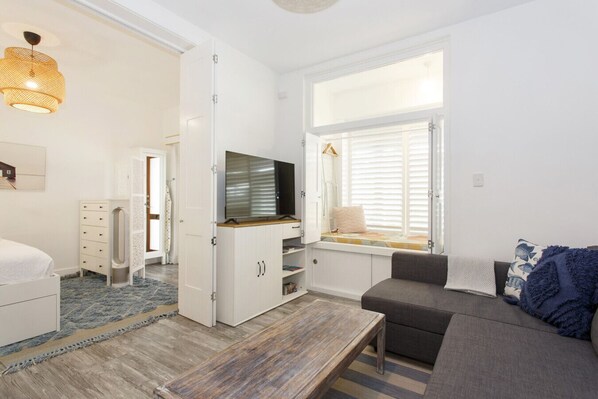 A modern living room with a sofa, a TV, a window with blinds, and a wooden coffee table. - Beach Shack Fremantle (Fremantle)