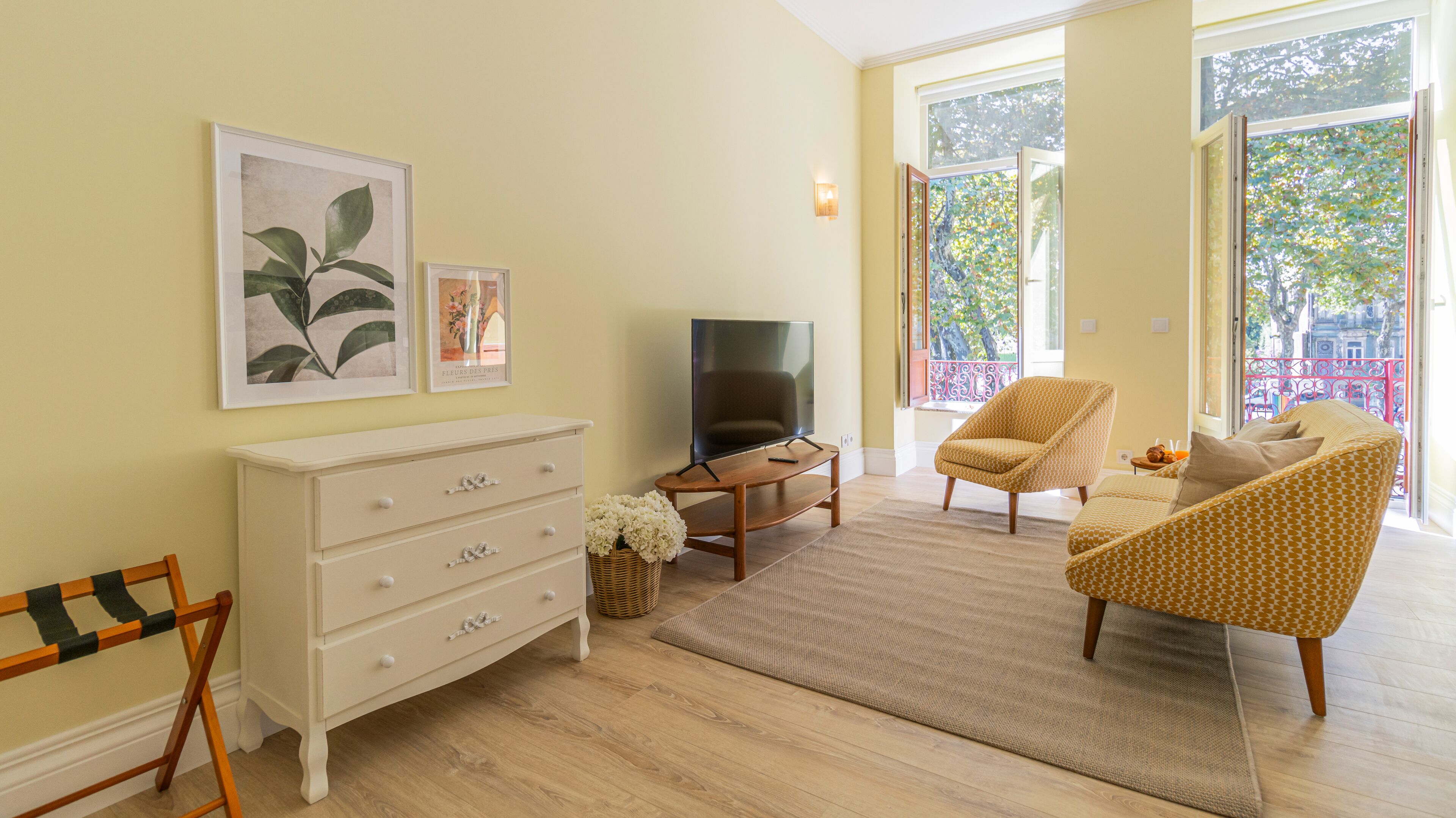 A living room with a TV, a sofa, a chair, a dresser, and a window with a view of trees.
